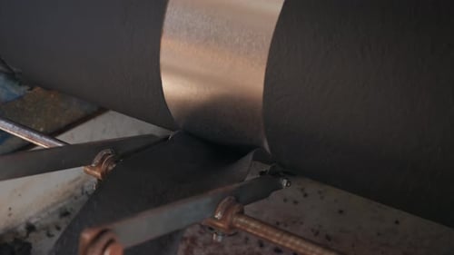 Closeup of dark sheet passing through metal rollers