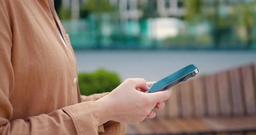 Side view of close up females hands using smartphone, typing a message or dialing number on the scre