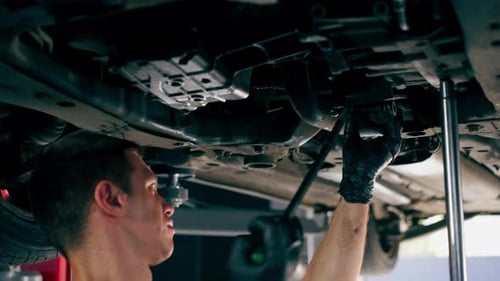 Close Up an Auto Mechanic at Service Station Checks a Car Being Lifted on a Lift Fixing Problems