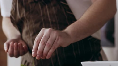 Professional Focused Chef Carefully Sprinkling Green Herbs Onto a Plate in Interior