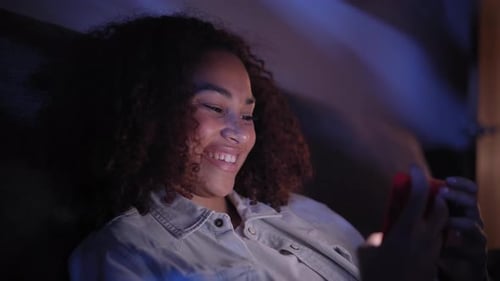 Mulher latina sorridente assistindo vídeos no celular relaxando em casa, jovem alegre e feliz