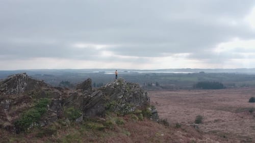 Hiker standing on top of a high rocky outcrop surrounded by stunning scenery