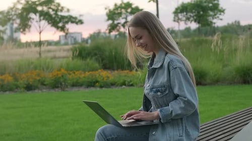 Woman Working on Laptop in the Park at Sunset