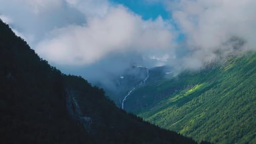 Aerial view of the wide green valley. White fluffy clouds float above and cast dark shadows on the l