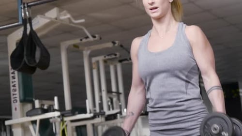 A fit blonde woman doing hammer curls with dumbbells at the gym