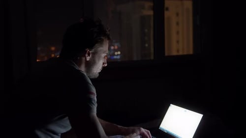 Hombre trabajando en una computadora portátil en una habitación oscura de hotel 4