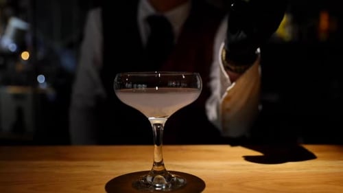 The bartender puts a slice of lemon into a finished drink on a lighted wooden bar while preparing to