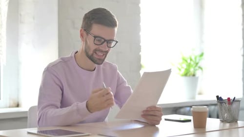 Excited Young Man Reading Documents and Cheering in Office