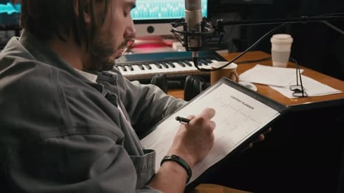 Young Male Music Podcast Host Writing Content Plan in Studio