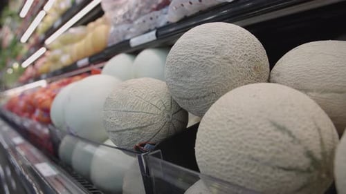 Différents melons à la peau lisse et rugueuse et d'autres fruits sur les étalages d'une épicerie.