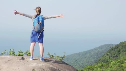 Female tourist with backpack raising hands on top of mountain