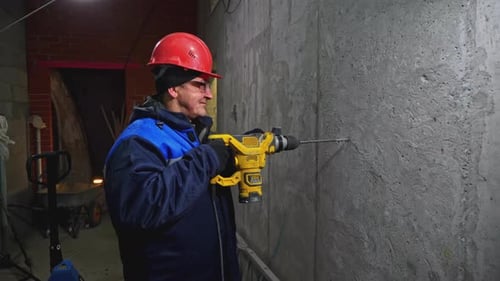 Un travailleur perce un mur en béton avec une pince à tournevis Un travailleur en uniforme perce un mur en béton avec perceuse