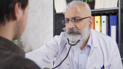 Mature Doctor Listens to Patient With Stethoscope
