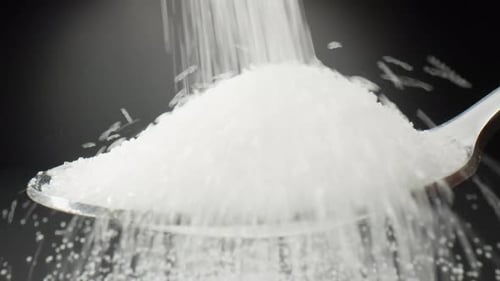 Pure white sugar cascades delicately into a spoon.