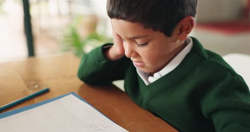 Bored, education and boy child doing homework, assignment or project in the dining room at home