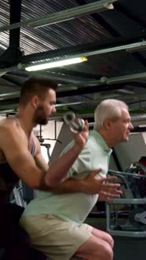 Senior Man Assisted With Squats in Gym