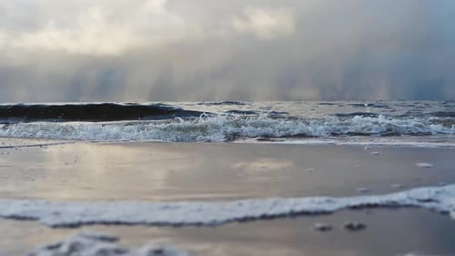 The small waves of the sea fight with the sand. Sea waves wash out the sandy shore. Rain clouds are