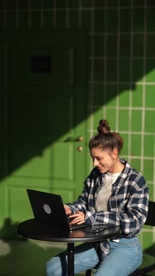 Schöne junge Frau, die mit Laptop im Café am Tisch sitzt und online arbeitet, tippt und lächelt