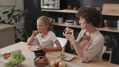 Mother and Daughter Eat Sandwiches in Kitchen