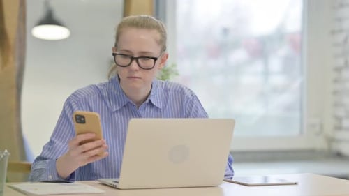 Woman Using Smartphone at Laptop Computer
