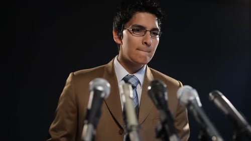 Man Speaking at Press Conference with Microphones