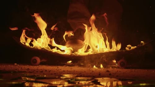Burning Skateboard Rests on Broken Glass at Night