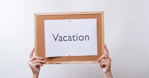 Die Hand der Frau zeigt das Papier an der Tafel mit dem Wort Vacation auf weißem Studiohintergrund mit Kopie sp