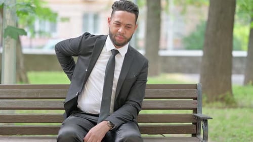 Man in Suit on Bench Sits with Back Pain