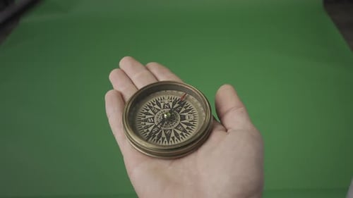 Travel Concept Magnetic Compass with a Rotating Arrow in an Open Male Palm on a Green Screen HDR
