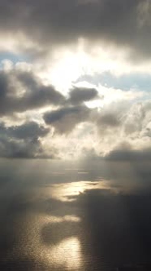 Vista vertical aérea: Rayos de sol que atraviesan dramáticas nubes de lluvia sombrías y malhumoradas sobre el mar