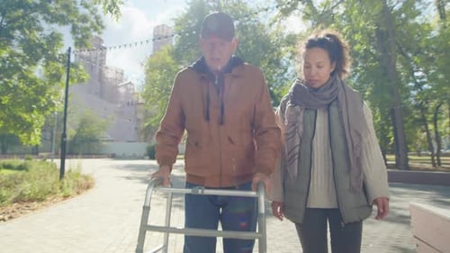 Caregiver and Senior Man with Walker Walking in Park