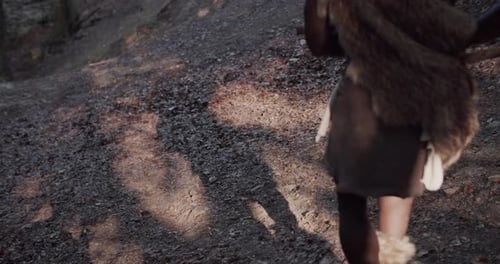 Rückenaufnahme eines Höhlenmenschen, der eine Waffe hält. Neandertaler tragen Tierhaut, stehen, sehen sich um, wollen