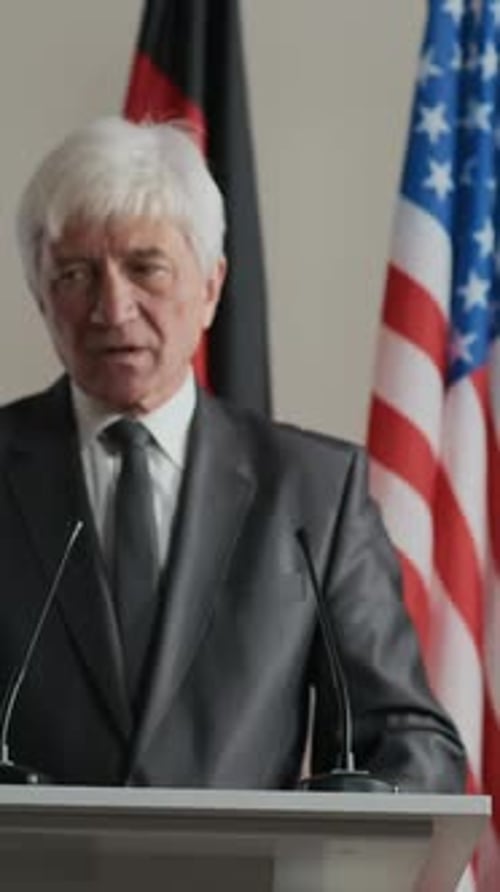 Adult Man Giving Speech with Flags Behind