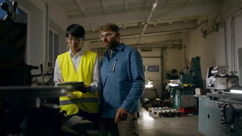 Japanischer Ingenieur kontrolliert älteren Arbeiter drinnen in einer Metallwerkstatt