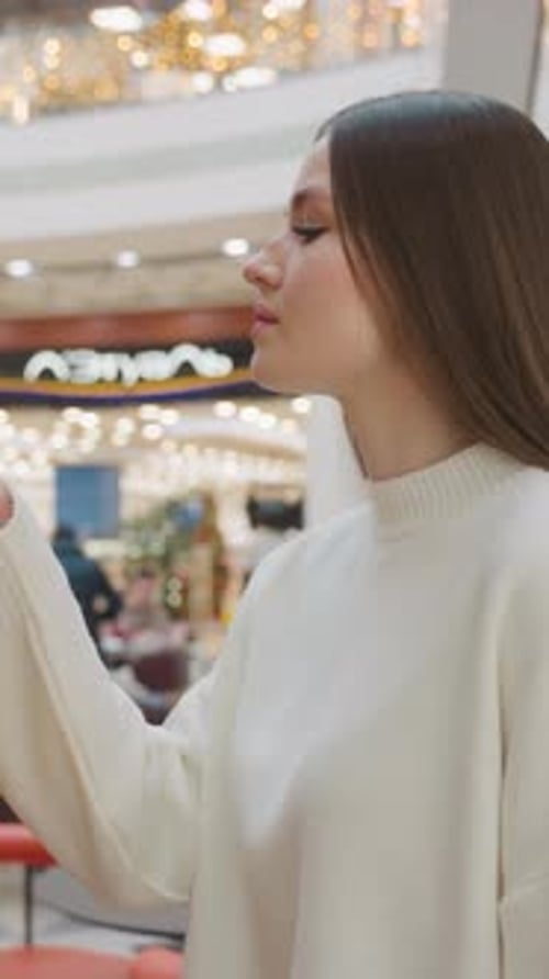 Lady Smelling While Admiring Decorative Plant with Lights in Shopping Mall Background