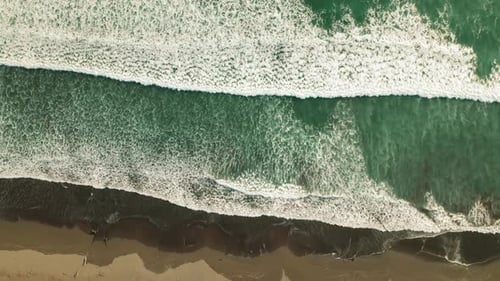 Top down view of ocean waves and sandy beach highlighting natural coastline