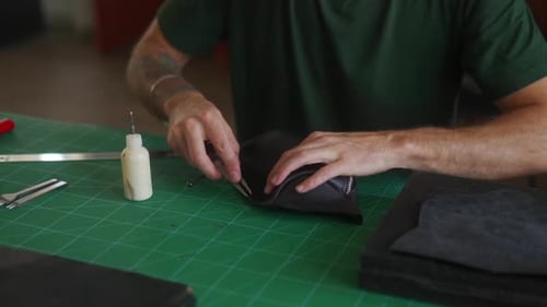 Close Up Shot of Professional Leather Craftsman's Hands at Work Table Making Cut on Black Handbag