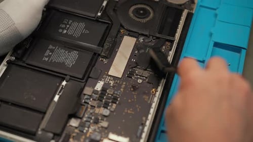Nahaufnahme eines nicht erkennbaren Technikers, der das zerlegte Laptop-Motherboard mithilfe einer Bürste reinigt