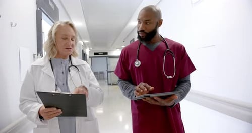 Diverse male and female doctors in discussion using tablet in hospital corridor, slow motion