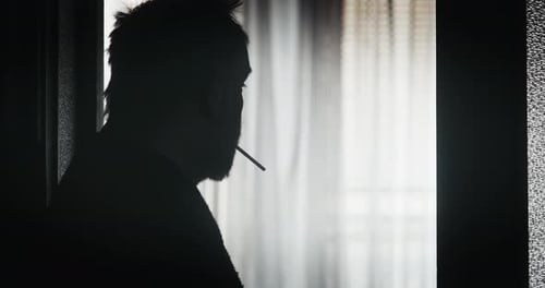 Silhouette of Man Lighting and Smoking Cigarette Indoors