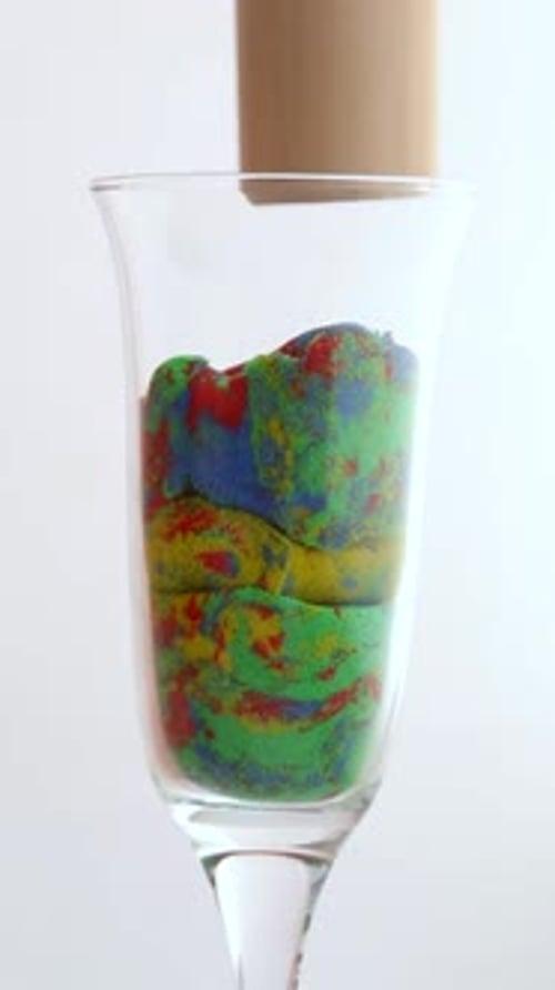 Multicolored Geometric Figures Made of Kinetic Sand are Crushed in a Glass Mug