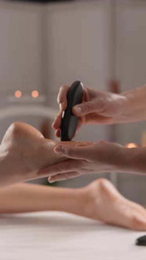 Gros plan d'un massothérapeute professionnel effectuant un massage relaxant des pieds aux pierres chaudes dans un environnement moderne