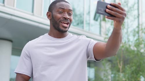 African American Man Holding Smartphone Having Video Chat on Urban Street in City Guy Blogger