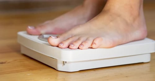 Bare Feet Stepping on White Bathroom Scale