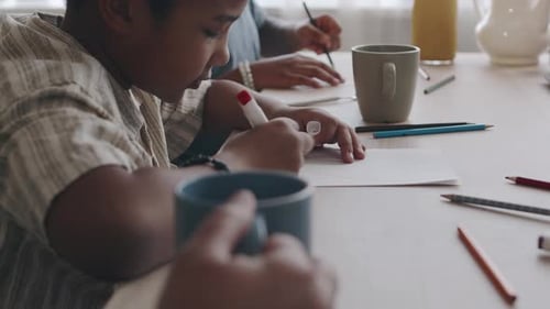 Schwarze Kinder sitzen am Tisch und zeichnen mit Farbmarkern und Stiften