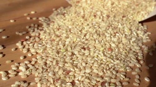 Slow movement from left to right. Brown rice on a wooden table. Close up. Raw rice out of the paper
