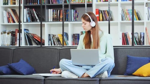 Teenager working on laptop and listening to music with headphones in library