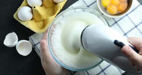 Frau verquirlt Eiweiß mit Handmixer am schwarzen Tisch, Ansicht von oben