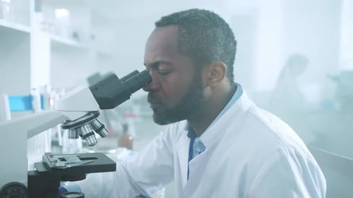 Portrait of African American Scientist Man in Uniform Looking Under a Microscope Turn Head to the