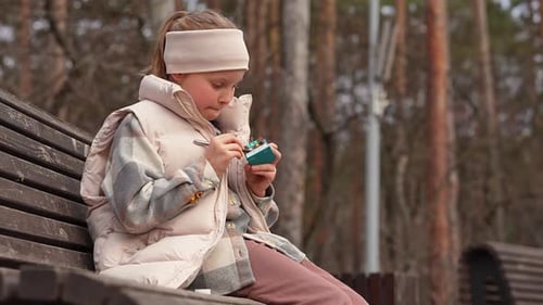 Young Caucasian Teenage Girl Sits on Bench in Park and Painting with Colors and Brush in Sketchbook